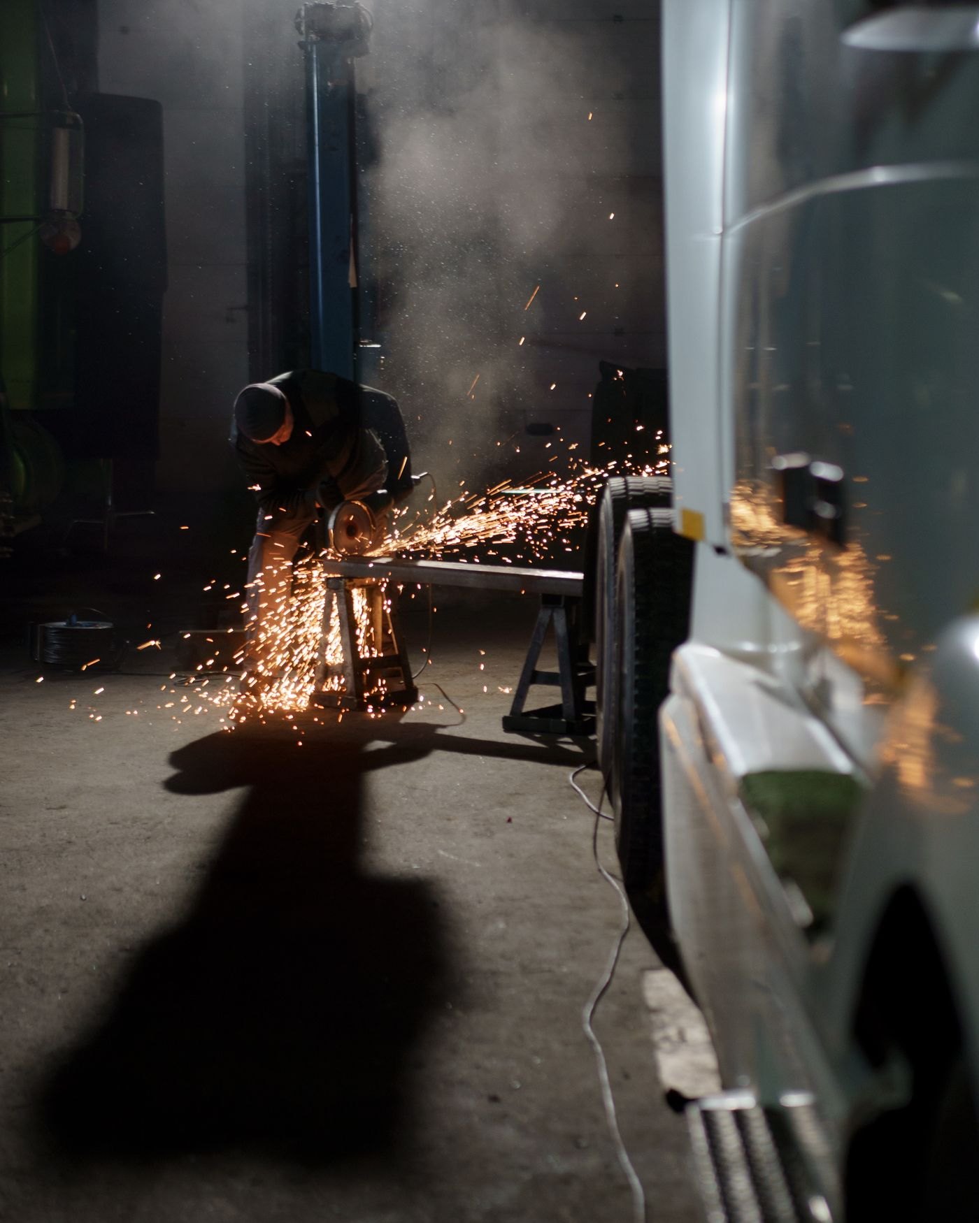 Grinder sparks next to a work truck in a shop