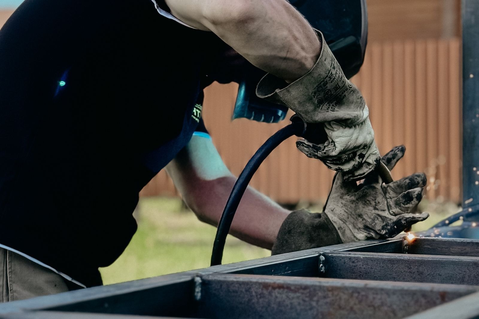 Welder joining a square-tube steel frame outdoors